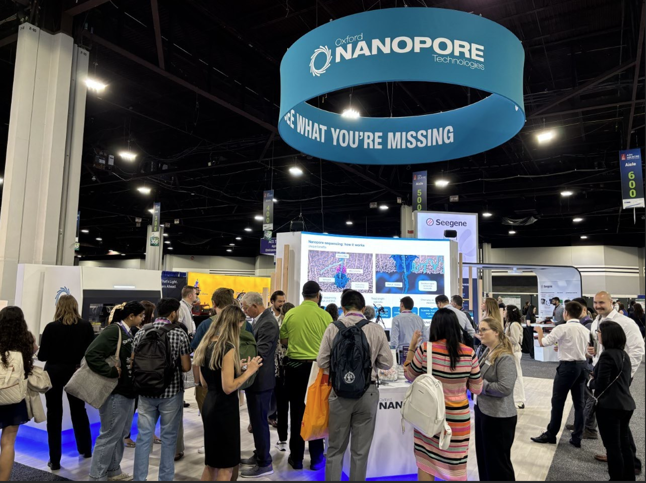 A busy booth at ASM Microbe 2024 with lots of people milling around with a large nanopore banner overhead