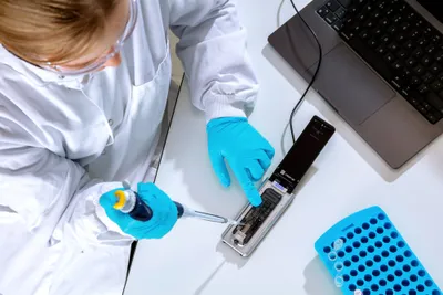 Image of a person loading a sample on to a MinION Flow Cell on a MinION Mk1D device, which is plugged into a laptop
