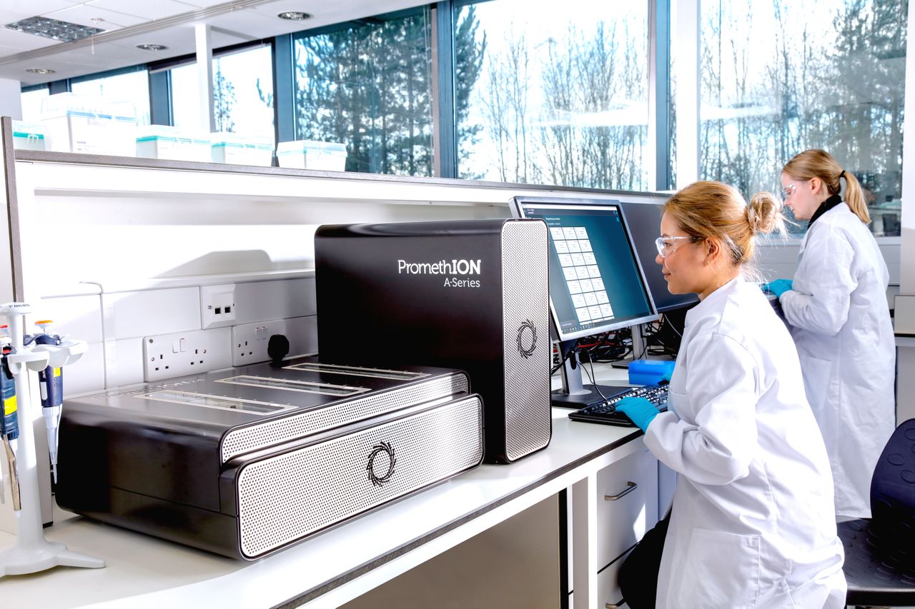 Image of a PromethION 24 in the lab next to two scientists