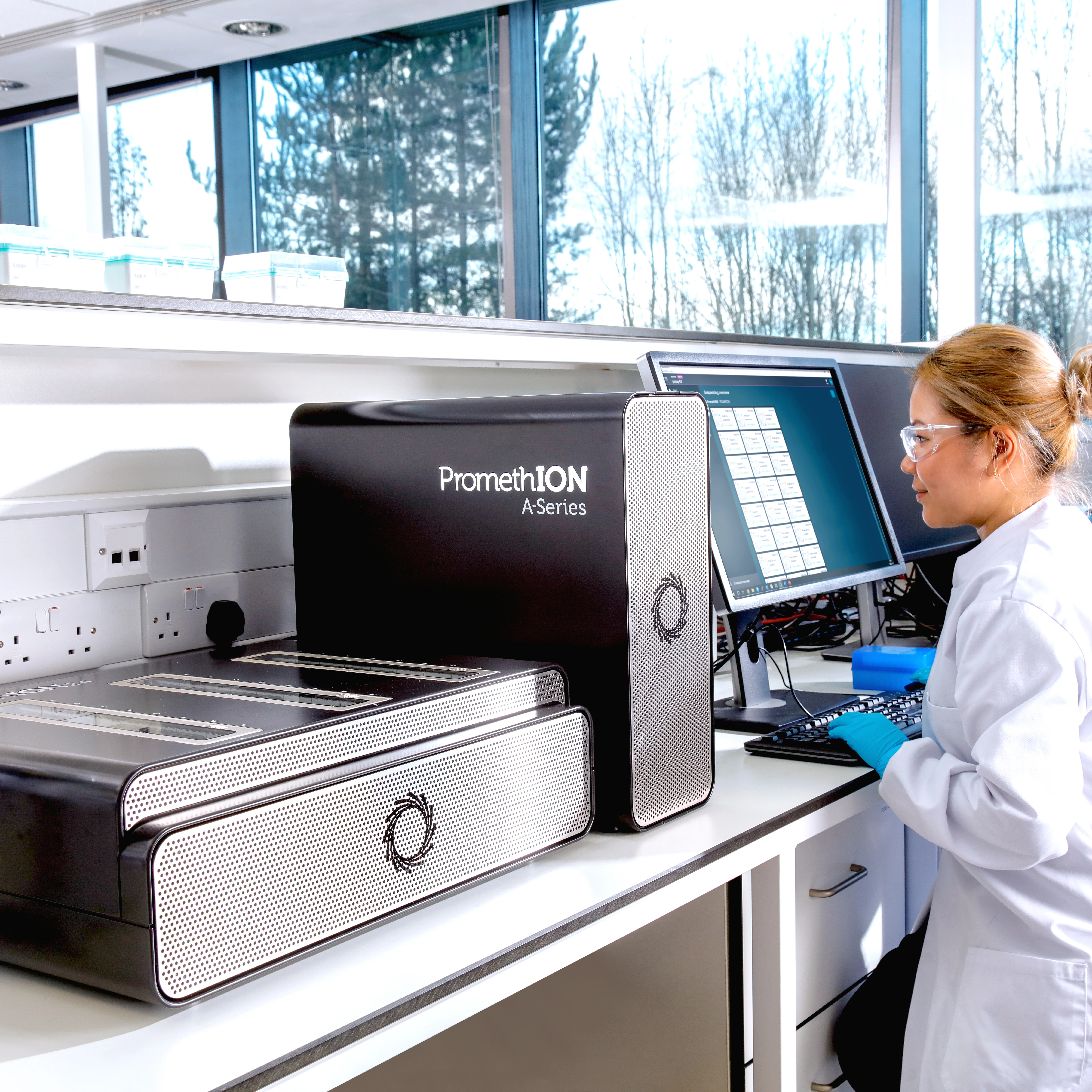 Image of a PromethION 24 in the lab next to two scientists